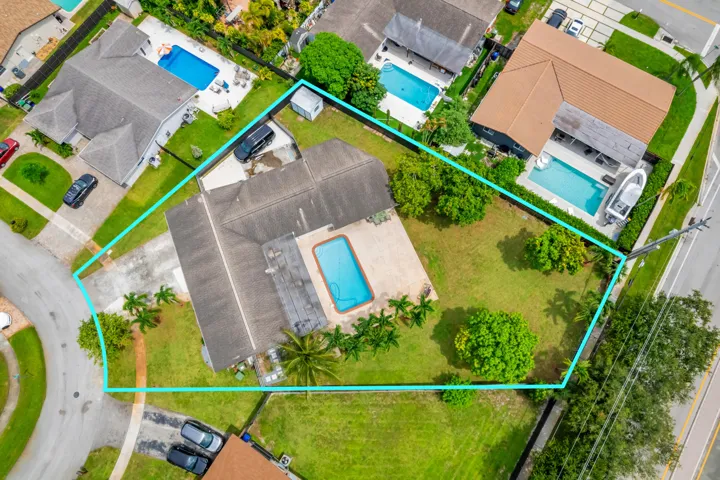 Aerial perspective showcasing the property with a private swimming pool, expansive green lawn, mature trees, and a concrete driveway
