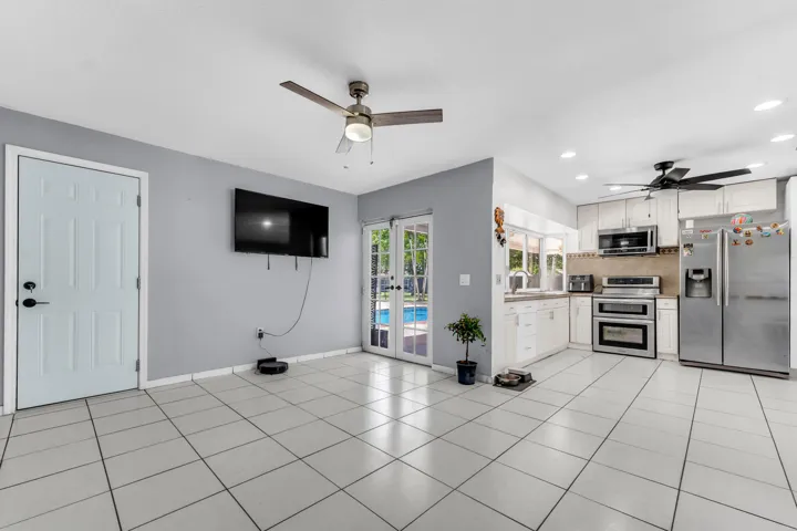 Open-concept living space featuring ceramic tile flooring, a kitchen with white cabinetry and stainless steel appliances, recessed lighting, and French doors opening to an outdoor area with a visible pool