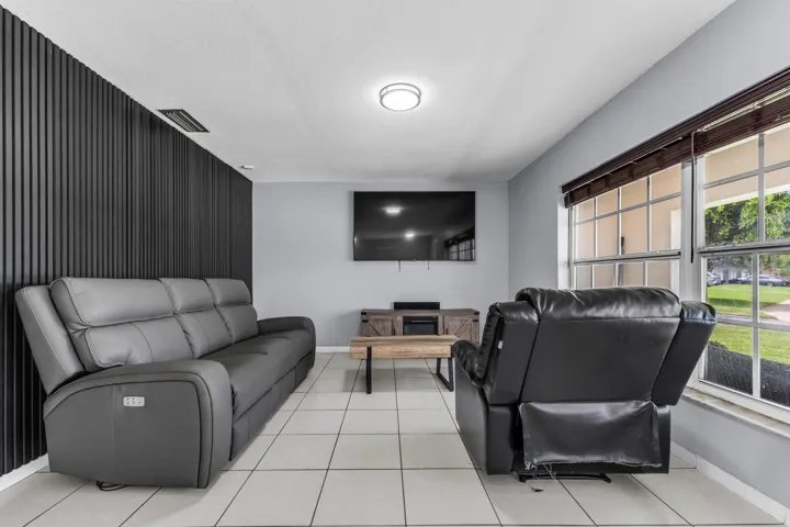 Living area featuring a modern accent wall, light tile flooring, and a large window with horizontal blinds