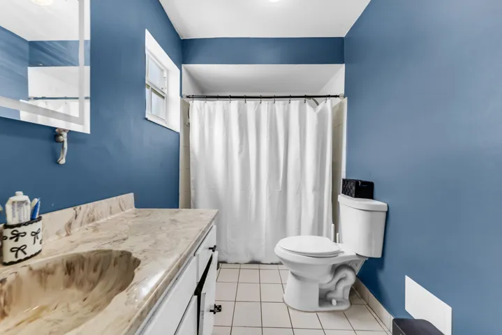 Bathroom located in 2nd primary bedroom featuring a vanity with a built-in sink and a patterned countertop, a toilet, and a shower area with a white curtain