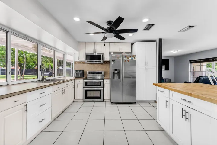 Kitchen featuring white cabinetry with dark hardware, stainless steel appliances, a ceiling fan with light, and white tile flooring