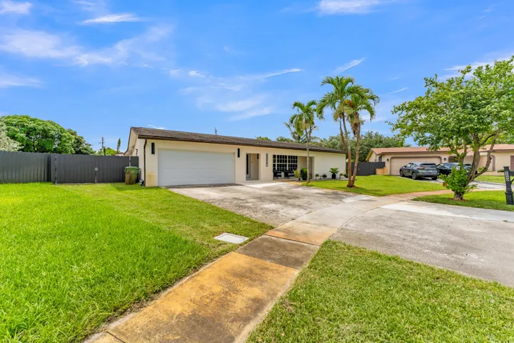 Single-story home featuring a two-car garage, front yard with mature trees, palm trees, and a concrete driveway