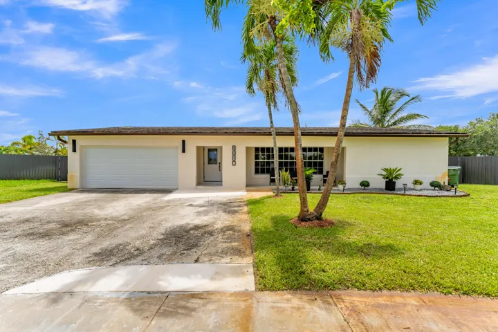 Single-story residence featuring a stucco exterior, an attached garage, a paved driveway, and a front lawn with mature palm trees