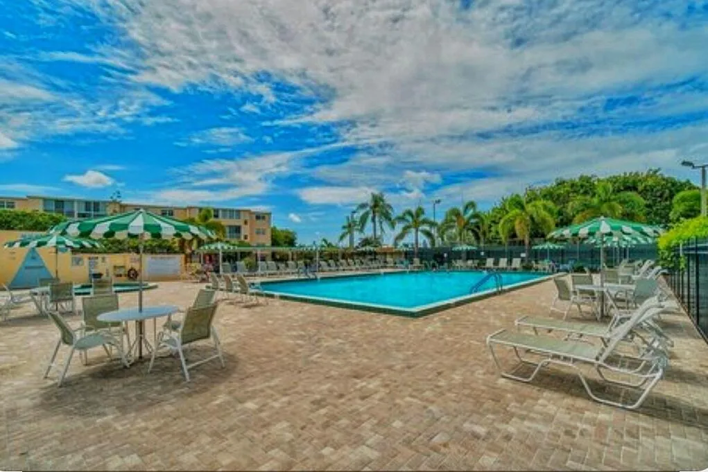 Expansive outdoor pool area featuring a rectangular swimming pool, paver deck, and surrounding palm trees