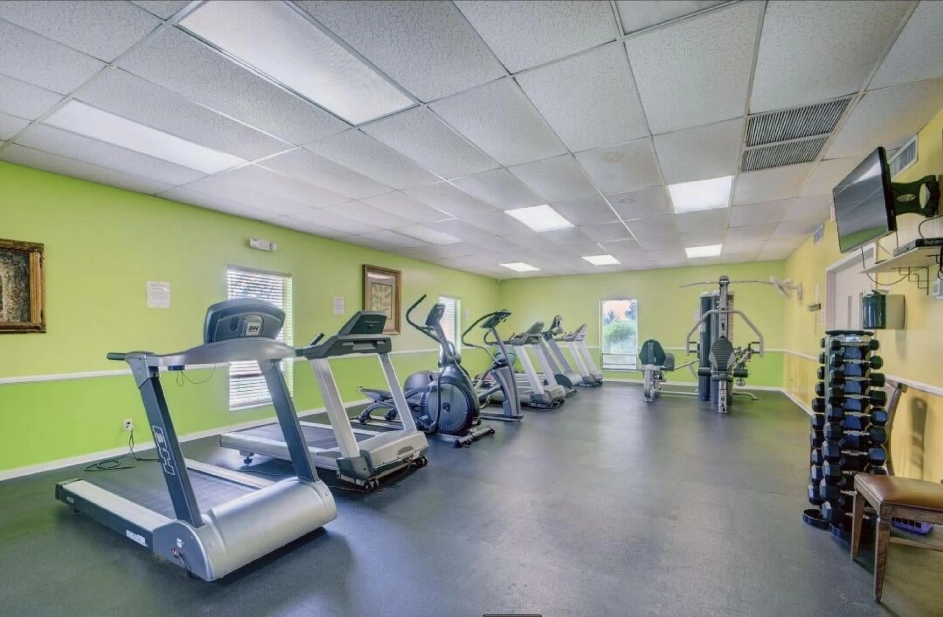 Fitness room featuring rubberized flooring, abundant overhead lighting, wall-mounted television, and multiple exercise machines