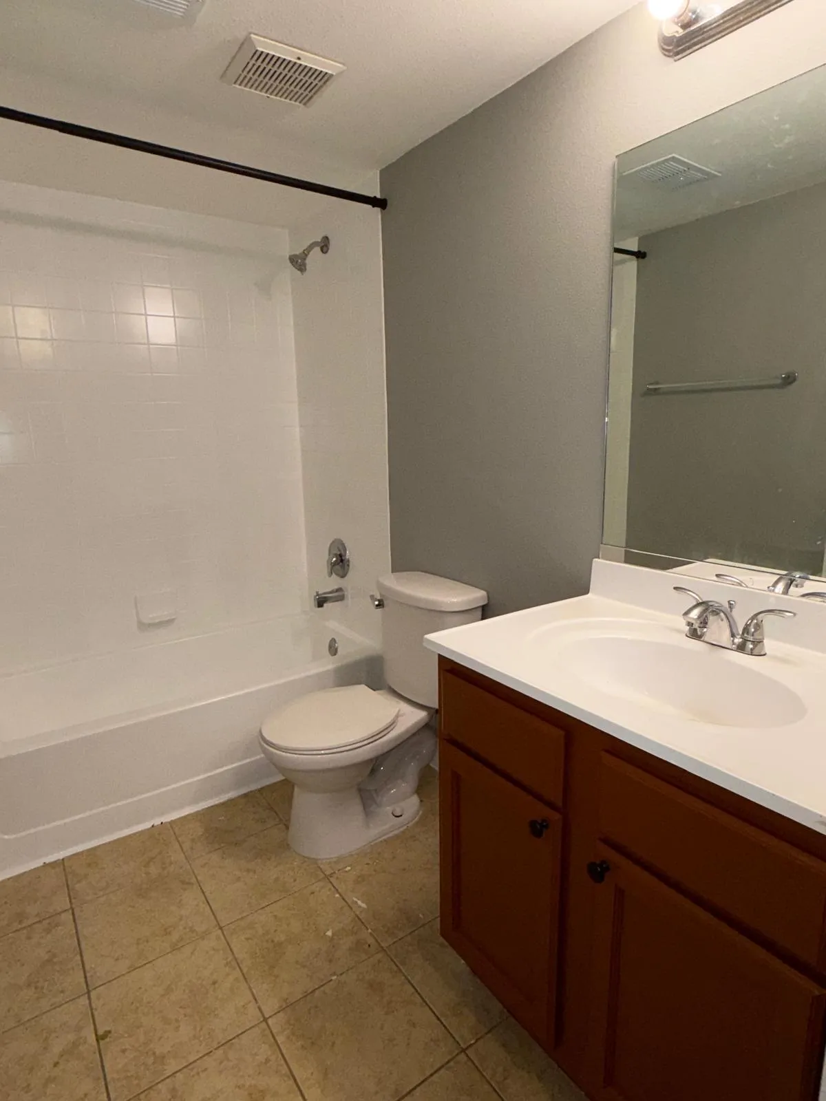 Bathroom featuring a white tub/shower combination, a brown vanity with a white countertop and integrated sink, and tiled flooring