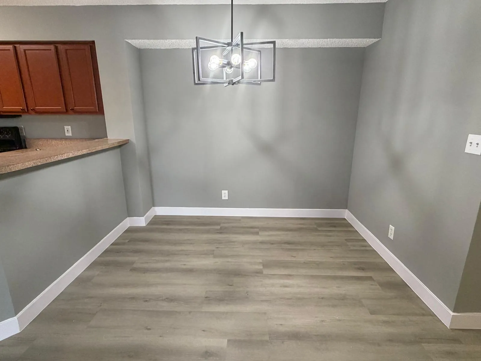 Dining area featuring light wood-finish flooring, a contemporary geometric chandelier, and a breakfast bar with a stone-finish countertop