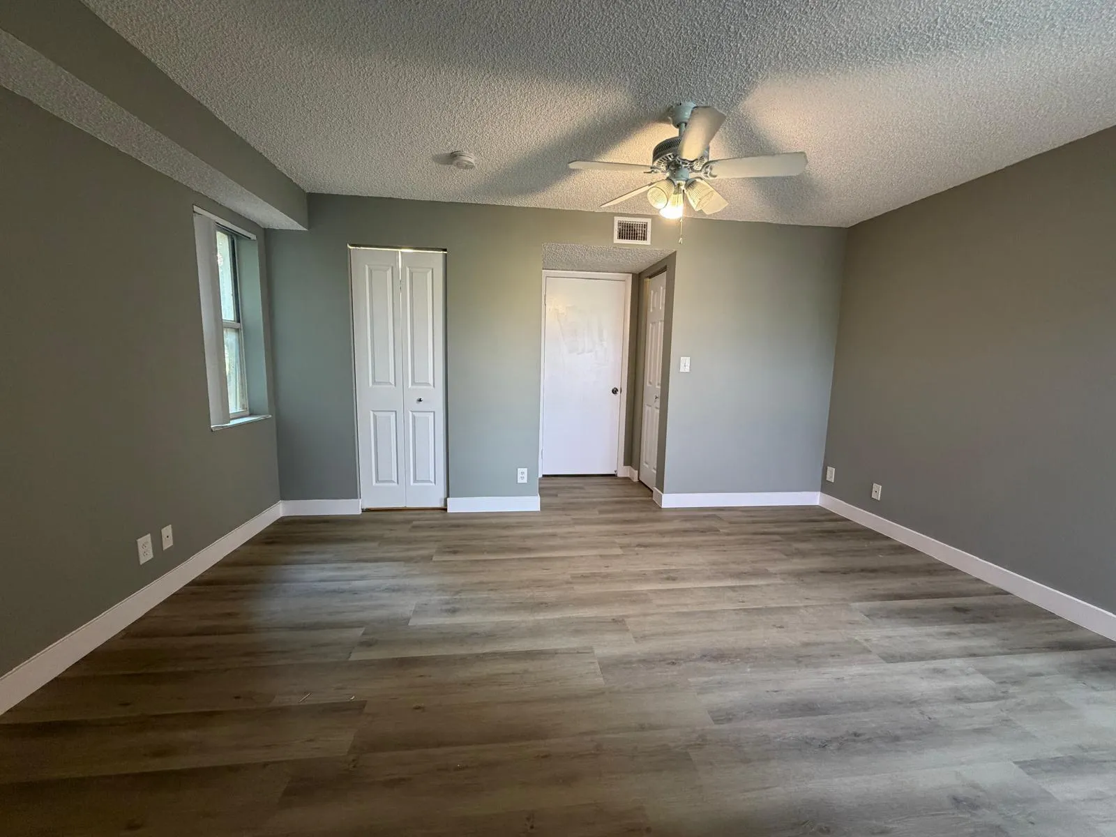 Spacious room featuring wood-finish flooring, neutral gray walls, white baseboards, and a ceiling fan with integrated lighting