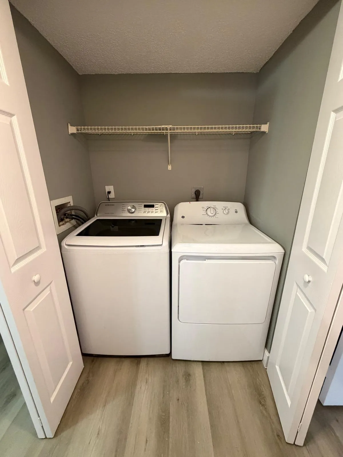 Dedicated laundry area featuring a wire shelving unit, wood-finish flooring, and bi-fold doors