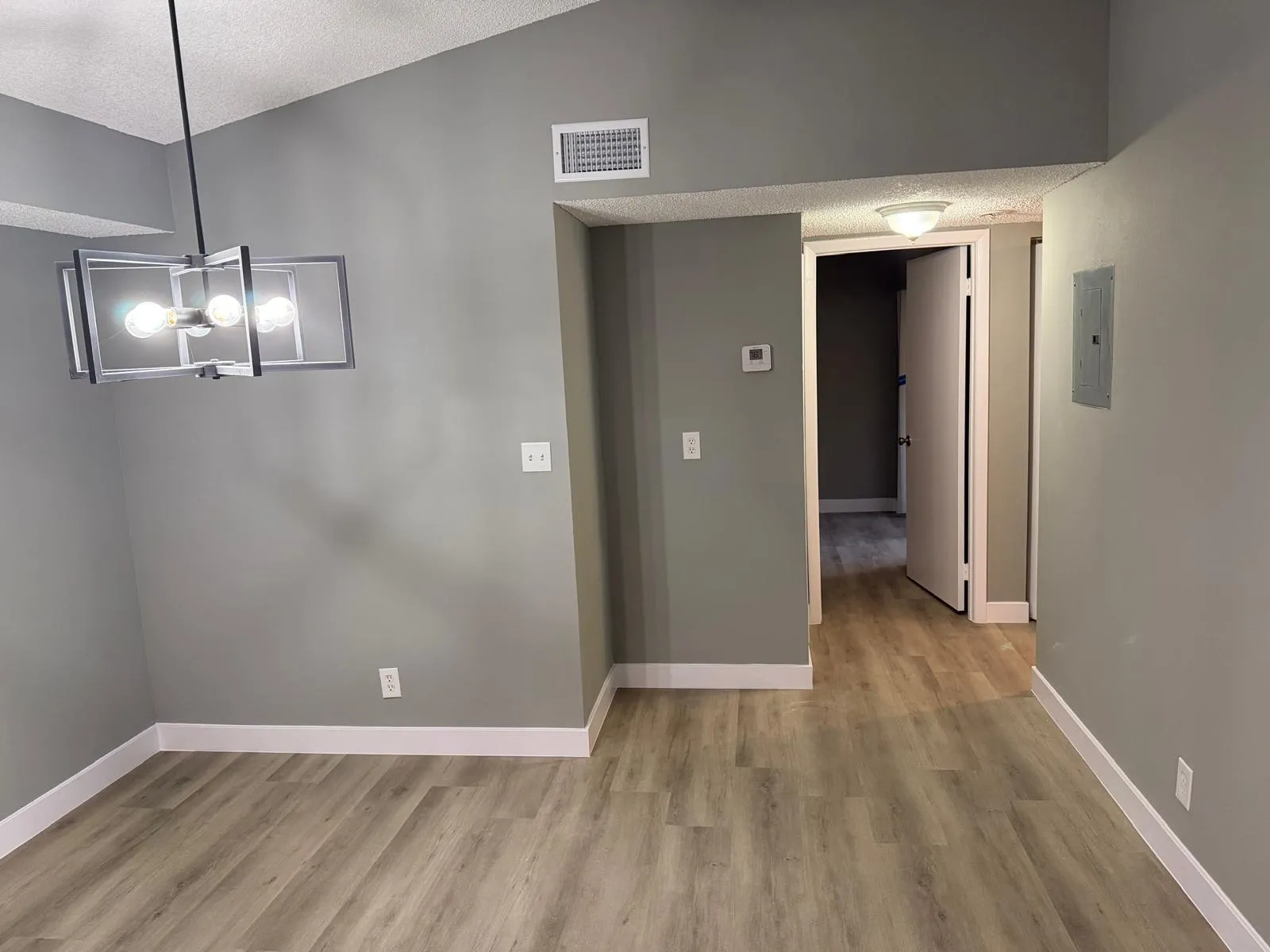Modern geometric chandelier illuminating a space with wood-finish flooring, vaulted ceiling, and neutral gray wall tones