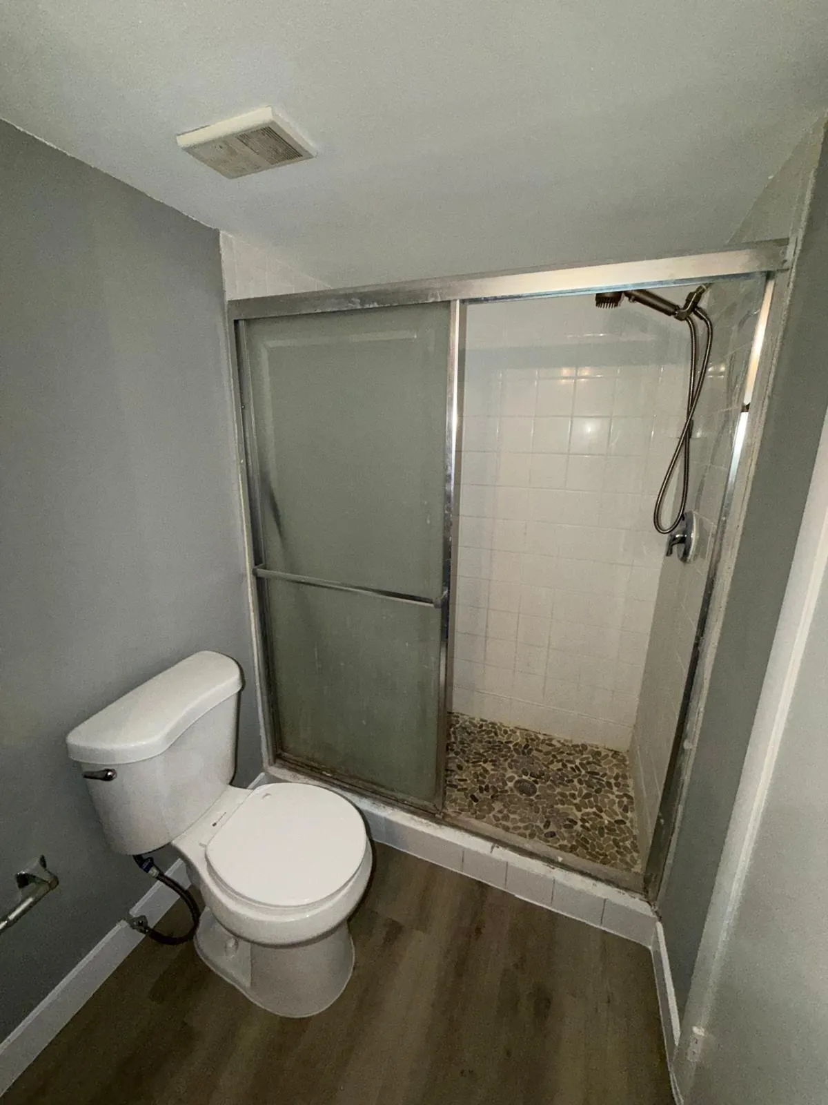 Shower with clear and frosted glass enclosure, white subway tile surround, and a pebble tile floor