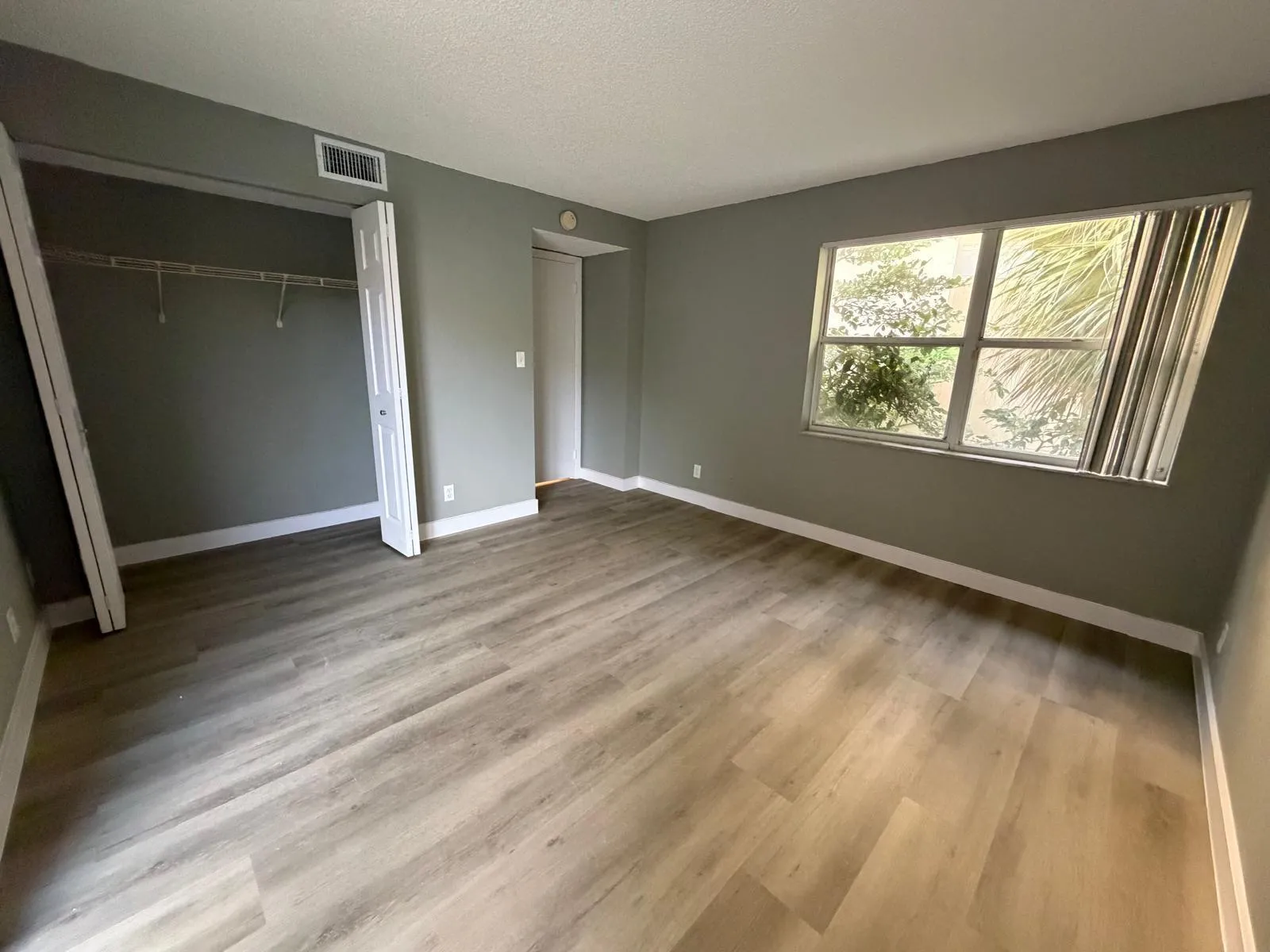 Spacious interior featuring wood-finish flooring, a bi-fold door closet with shelving, a large window, and light gray wall paint