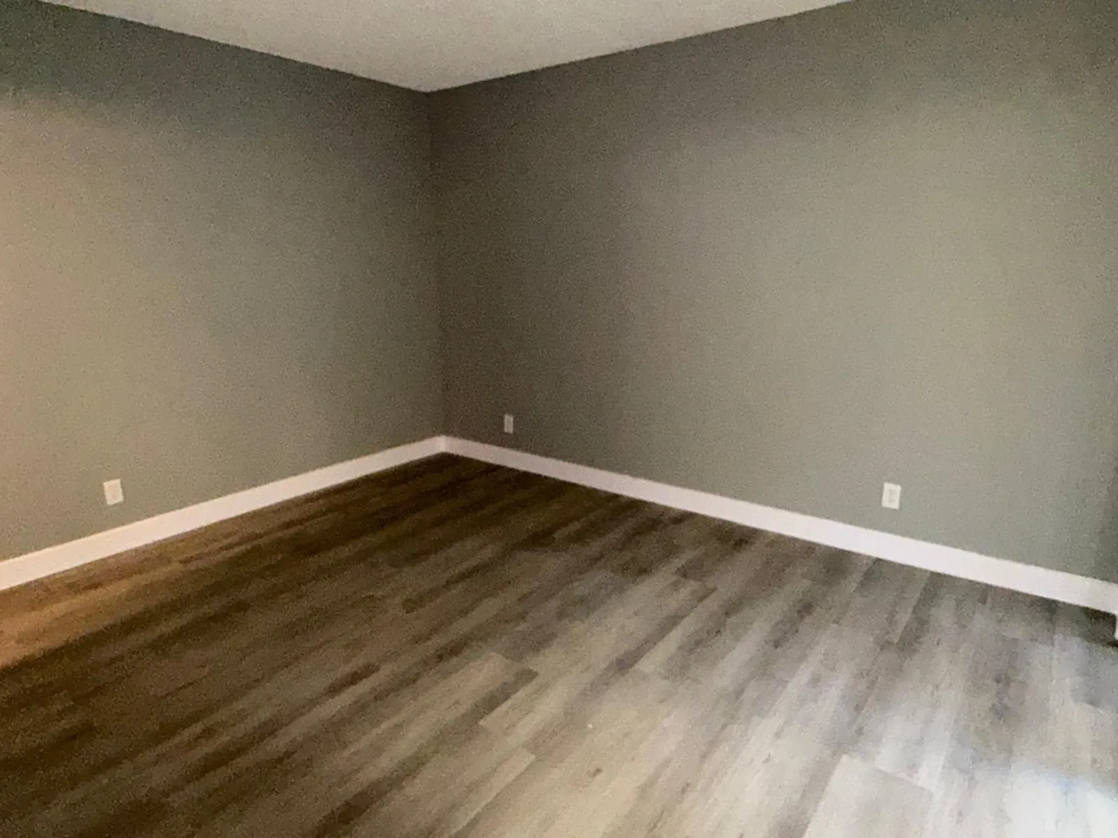 Wood-finish flooring with varying plank widths, light gray wall paint, and white baseboards