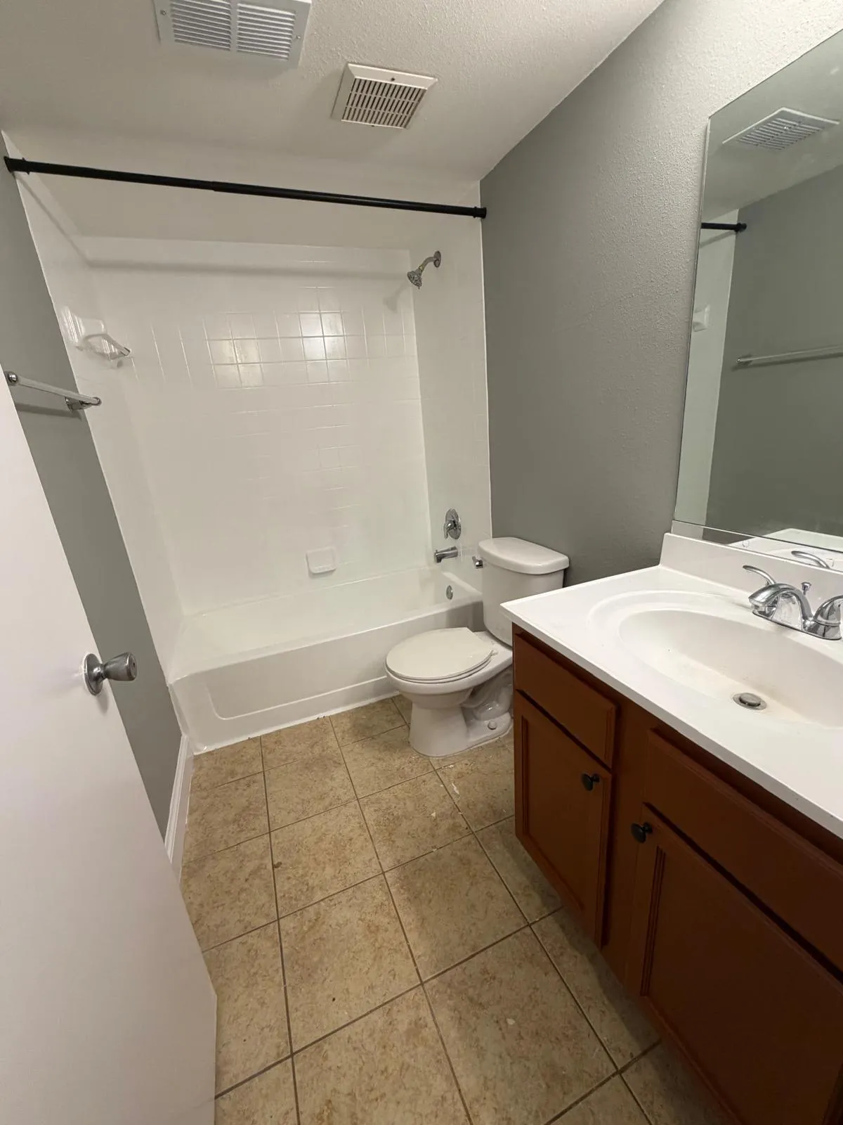 Full bathroom featuring a white tub/shower combination, a brown wood-finish vanity with an integrated sink, a wall-mounted mirror, and tile flooring