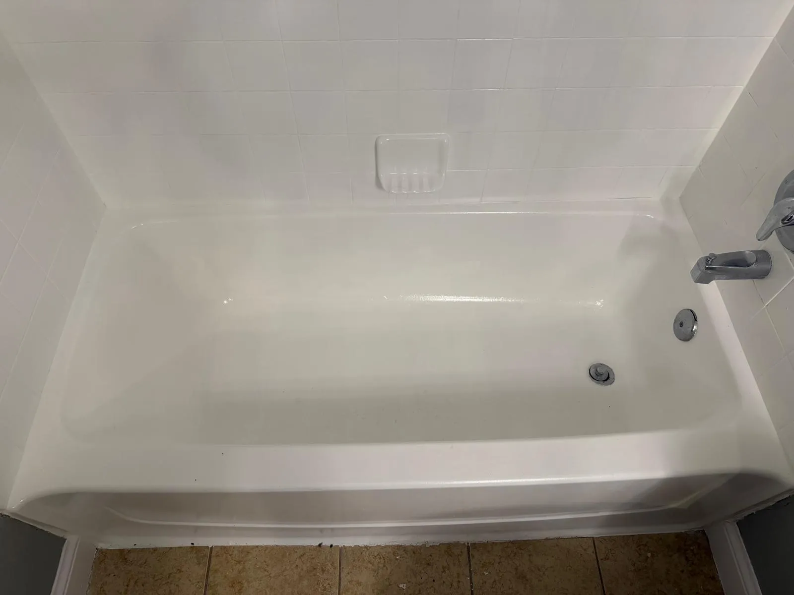 White bathtub with integrated soap dish, chrome fixtures, and white subway tile surround
