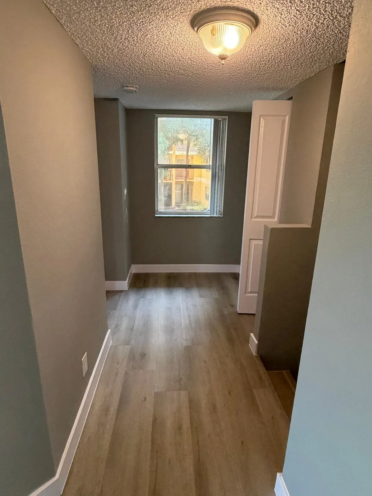 Hallway featuring wood-finish flooring, a window, baseboard molding, a flush mount ceiling light, and neutral wall tones