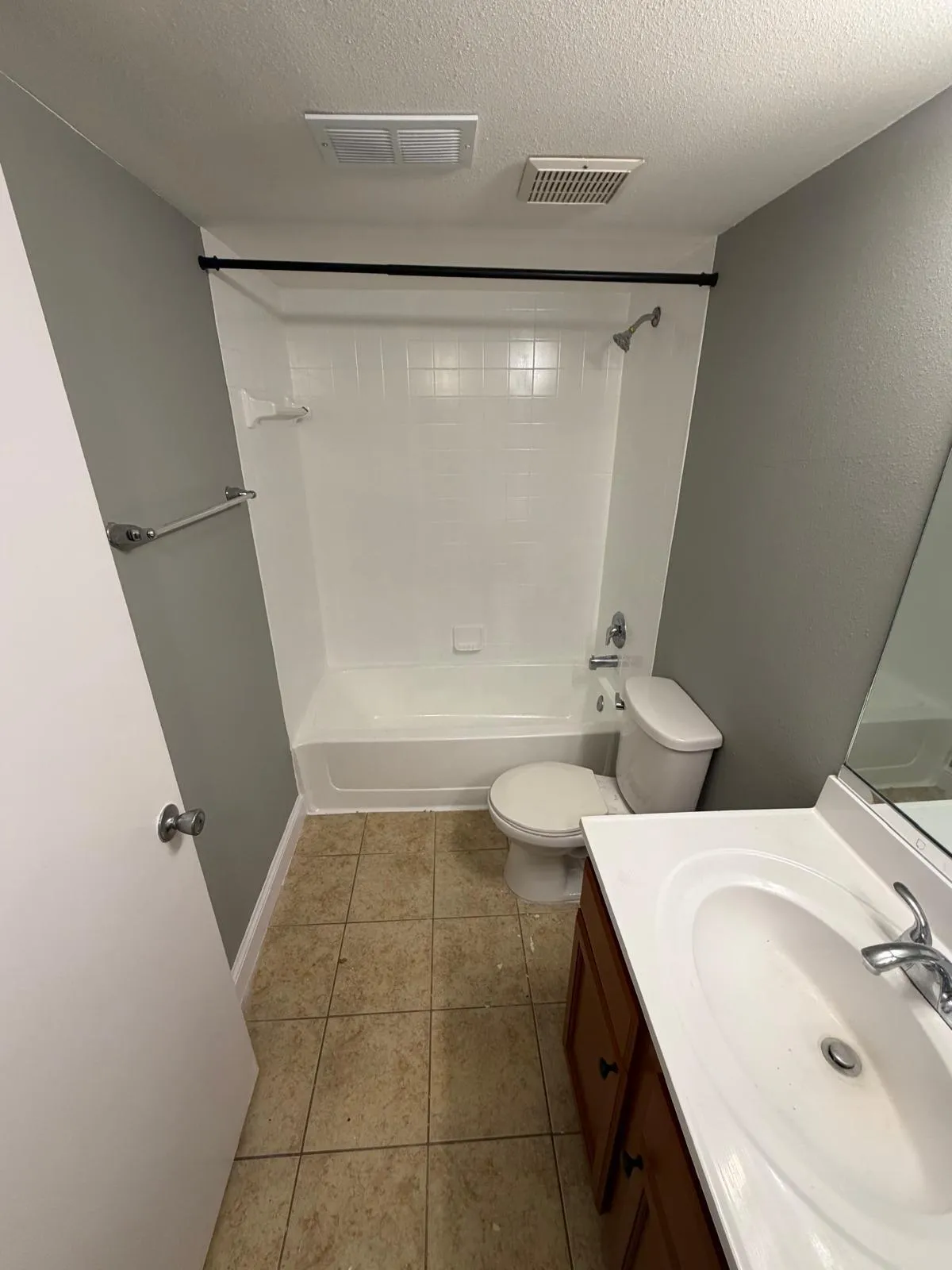 Bathroom featuring a white tub and shower combination with a black shower rod, a white toilet, and a vanity with a white sink and wood-finish cabinetry