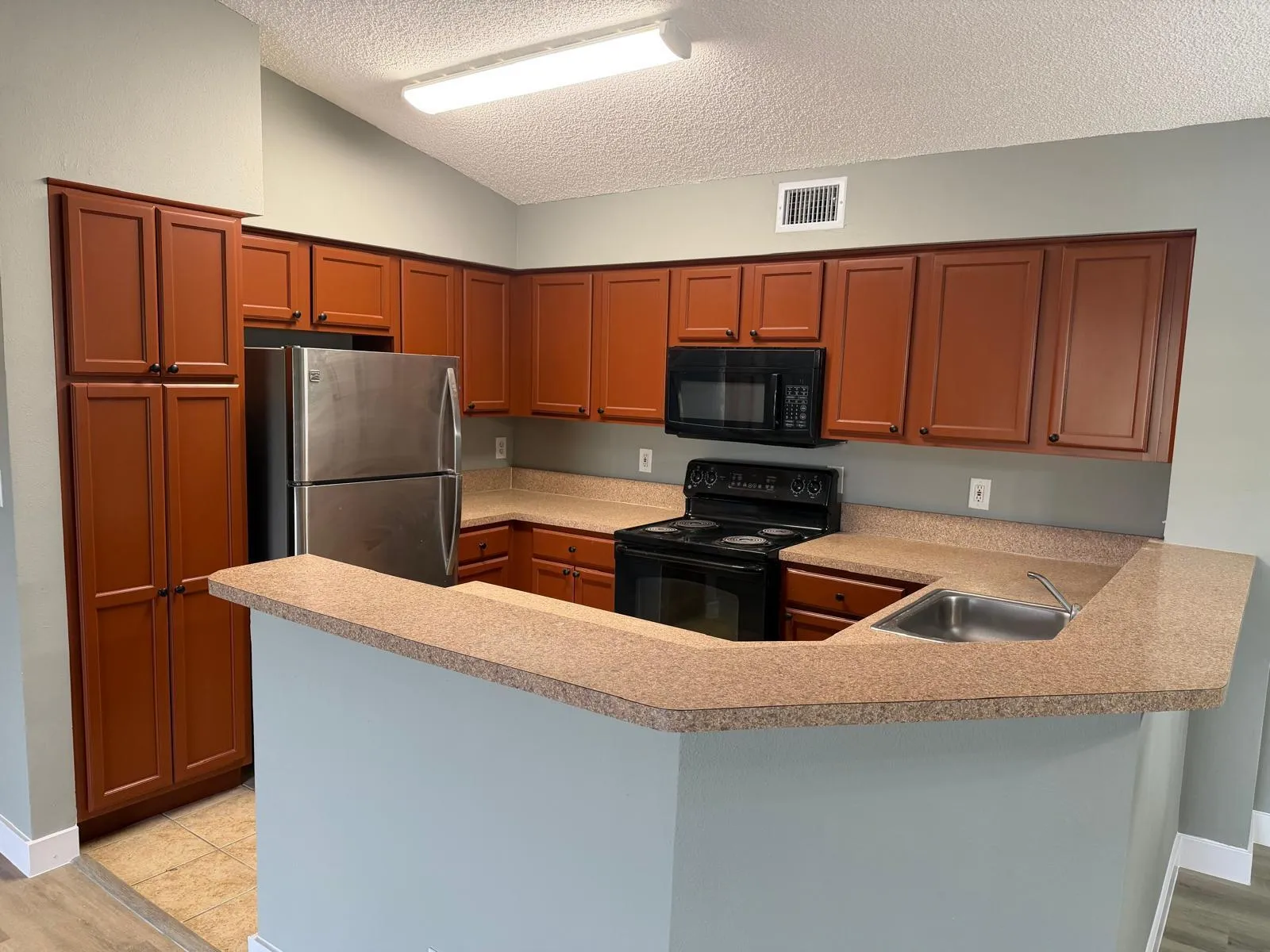 Kitchen featuring wood-finish cabinetry, stainless steel refrigerator, black range, black microwave, and a breakfast bar with an integrated sink