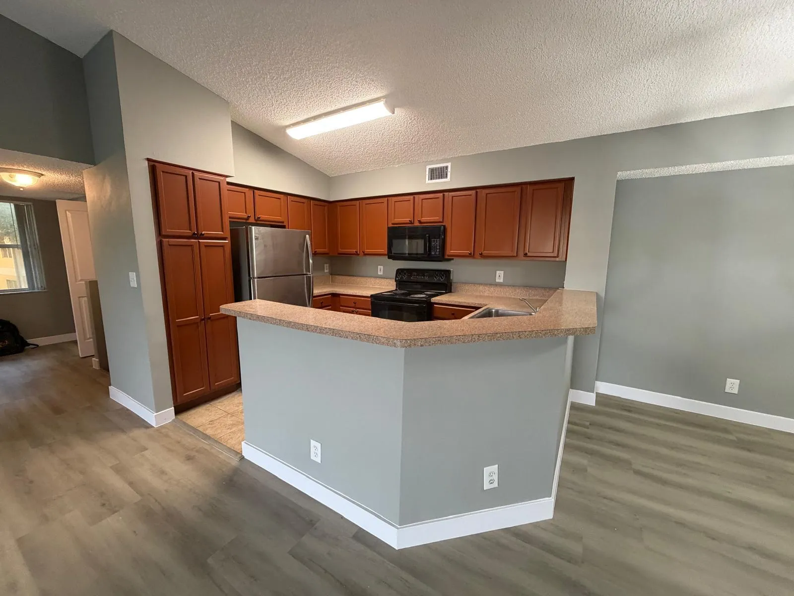 Kitchen featuring wood-finish cabinetry, stainless steel refrigerator, black range, and an integrated breakfast bar with a neutral countertop