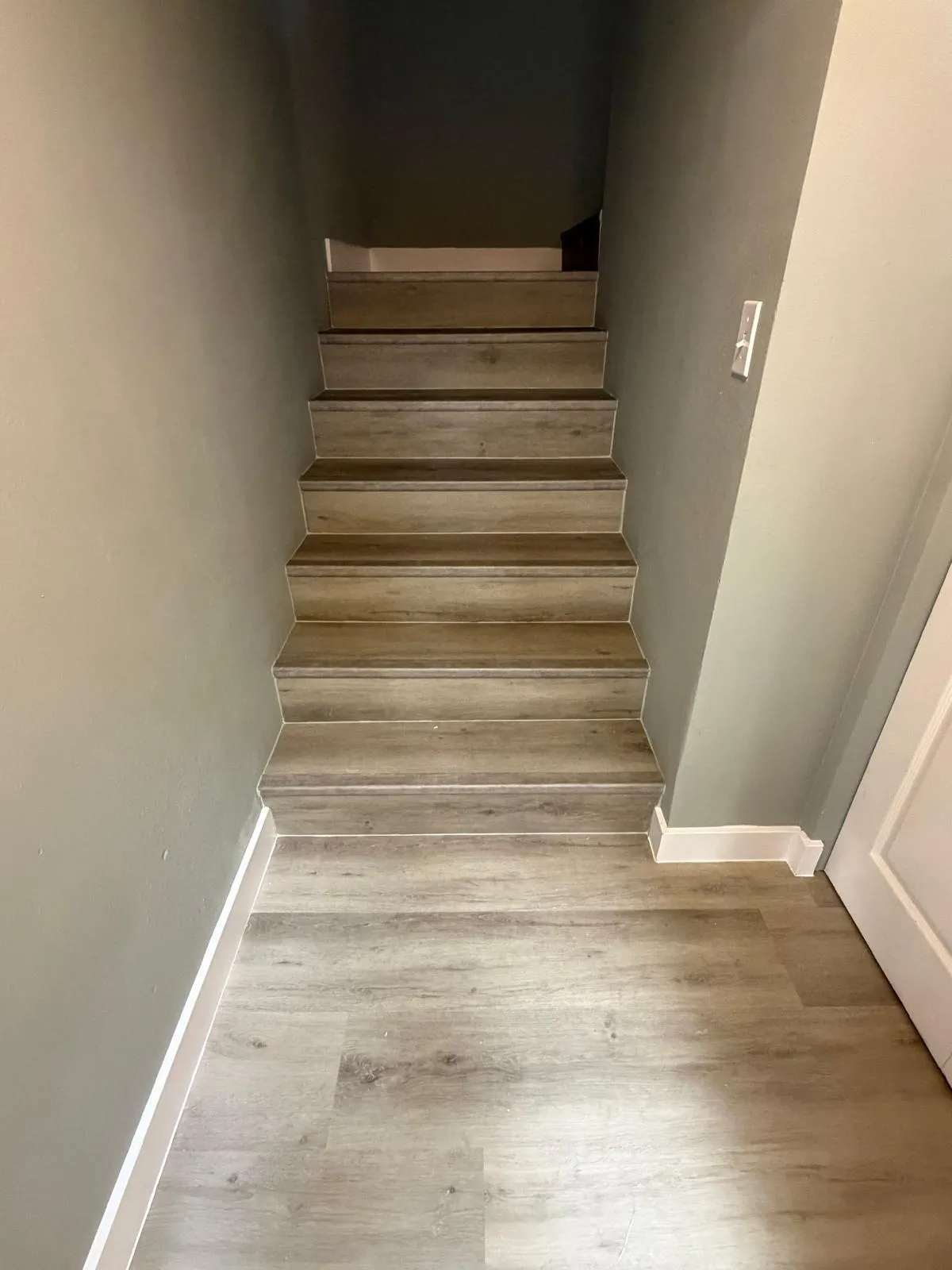 Staircase featuring wood-finish flooring, light grey wall paint, white baseboards, and a framed doorway