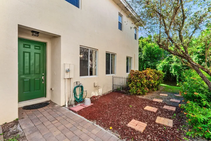 Cream stucco exterior featuring a green entry door and brick paver walkway