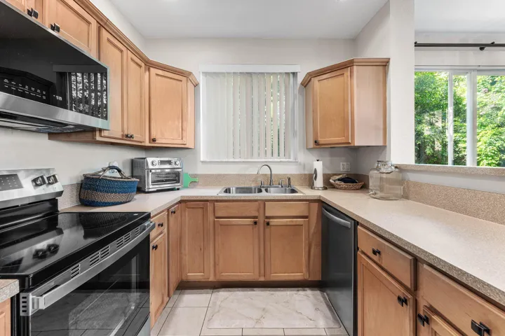 U-shaped, open kitchen featuring light wood cabinetry, light-colored countertops and a window over the kitchen sink