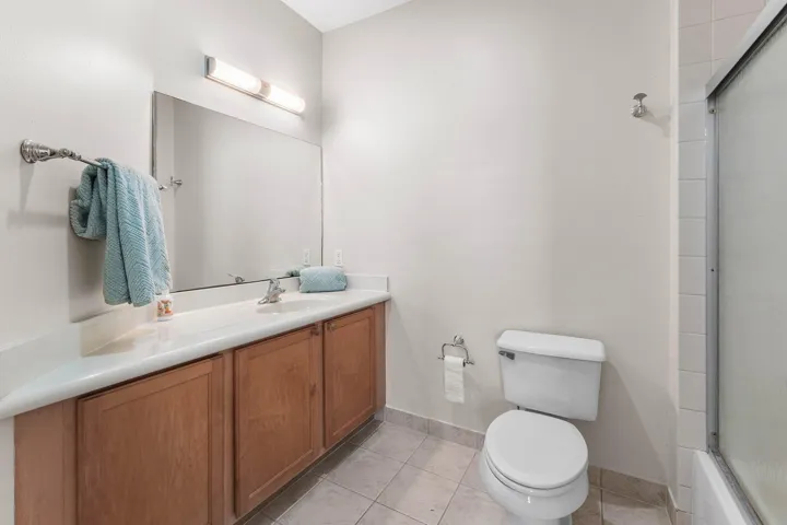Bathroom featuring a wood-finish vanity with a light-toned countertop, a rectangular mirror, and an overhead light fixture with a tub/ shower combination.