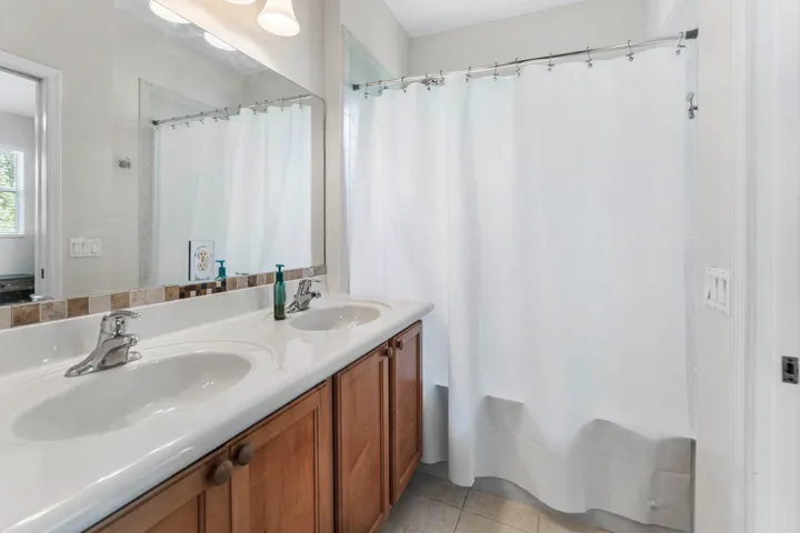 Dual vanity featuring integrated white sinks, chrome faucets, and wood-finish cabinetry with round knobs and a tub.