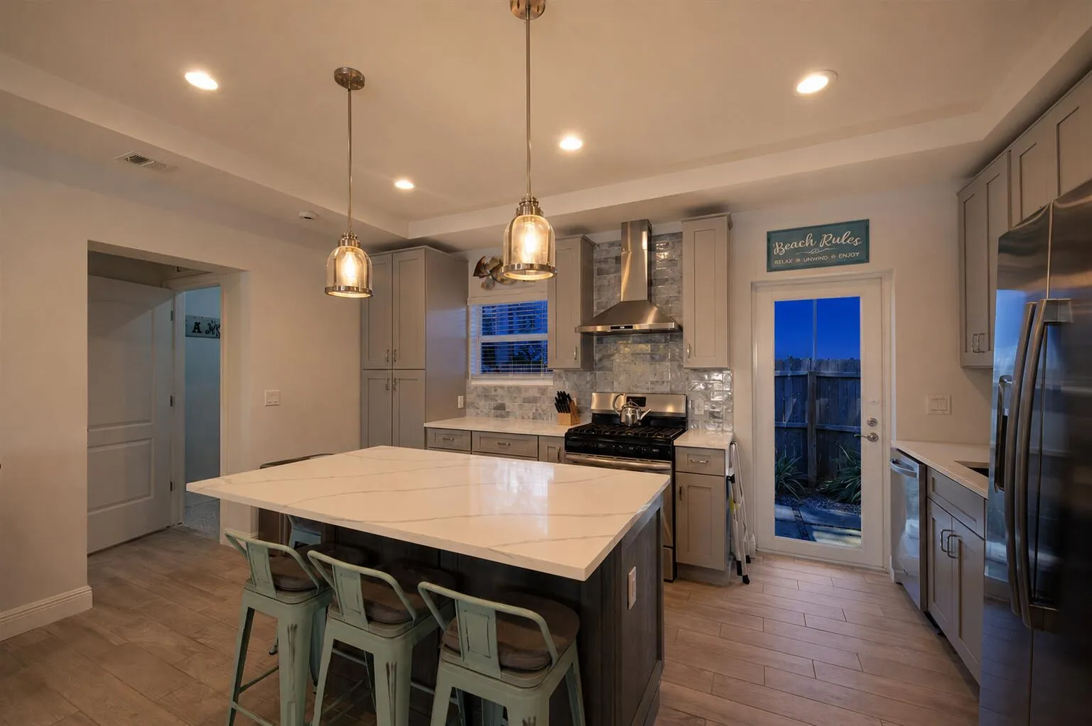 Kitchen featuring an island with a light-toned countertop, pendant lighting, stainless steel appliances, light wood-finish flooring, and a glass-paneled door