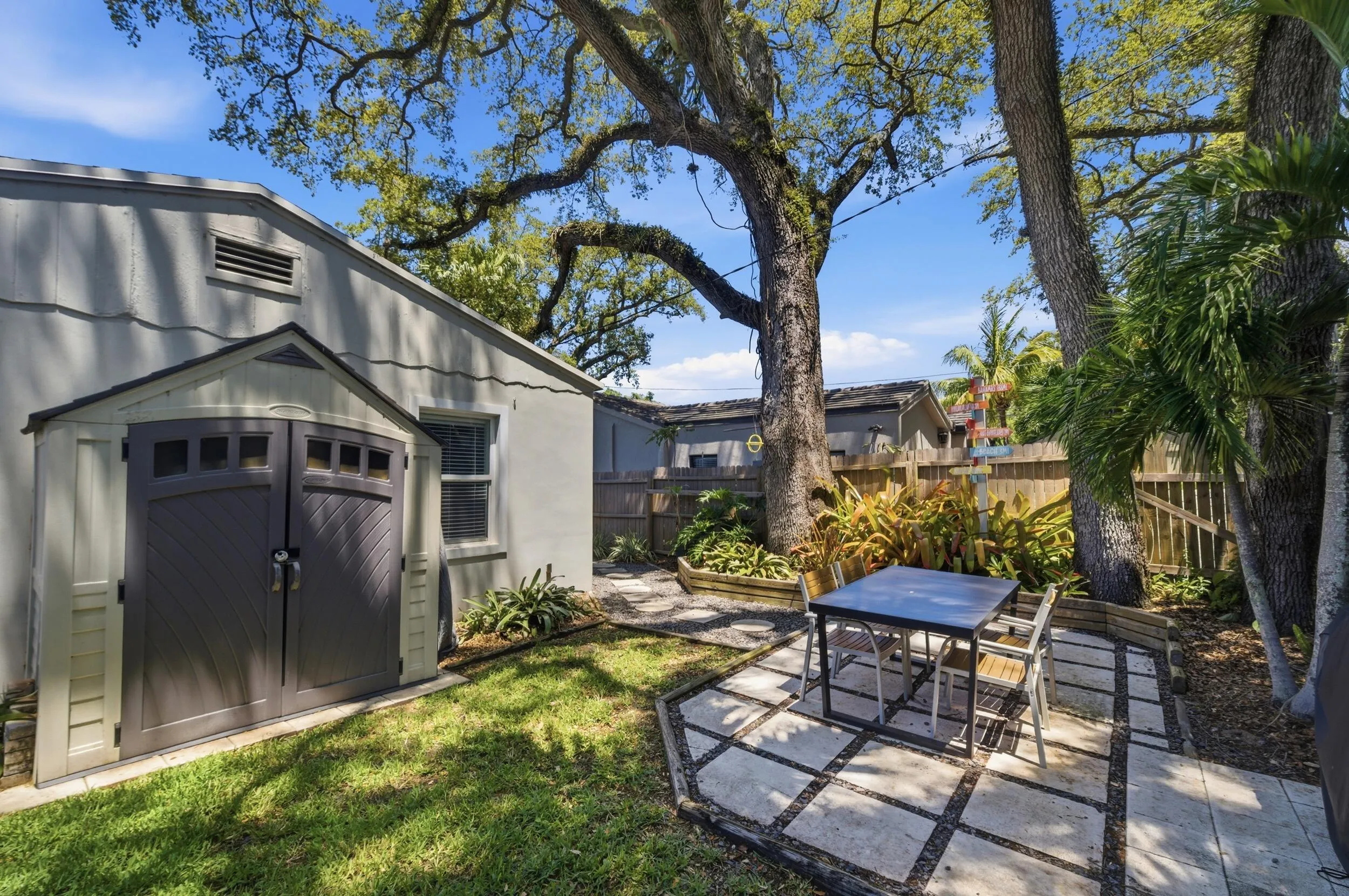 Private backyard featuring a paver patio with a dining area, lush landscaping, mature trees, and a storage shed