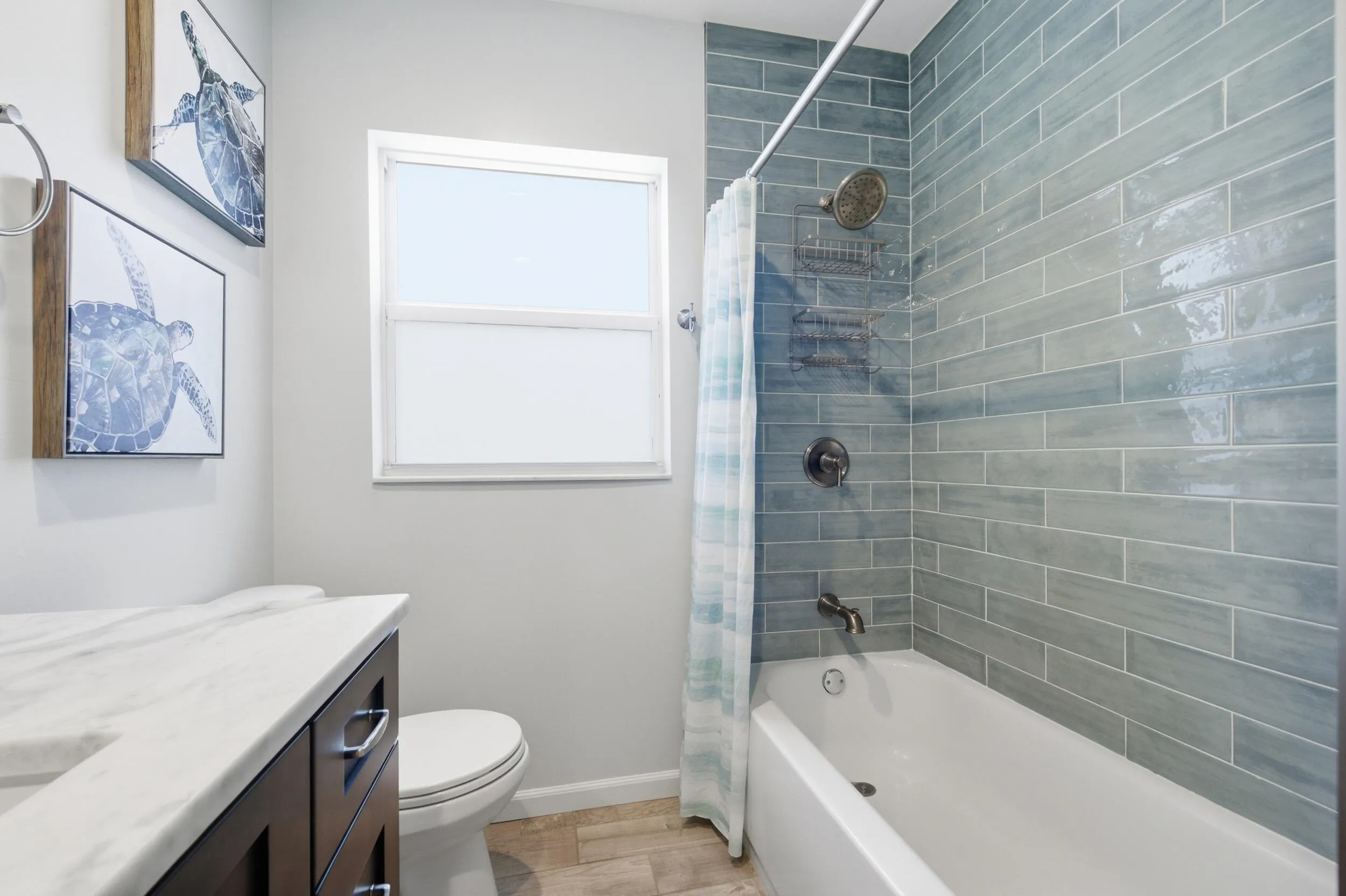 Bathroom featuring a tiled shower and bathtub combination with a rain showerhead, a window, a white toilet, a dark wood-finish vanity with a white countertop, and wood-finish flooring