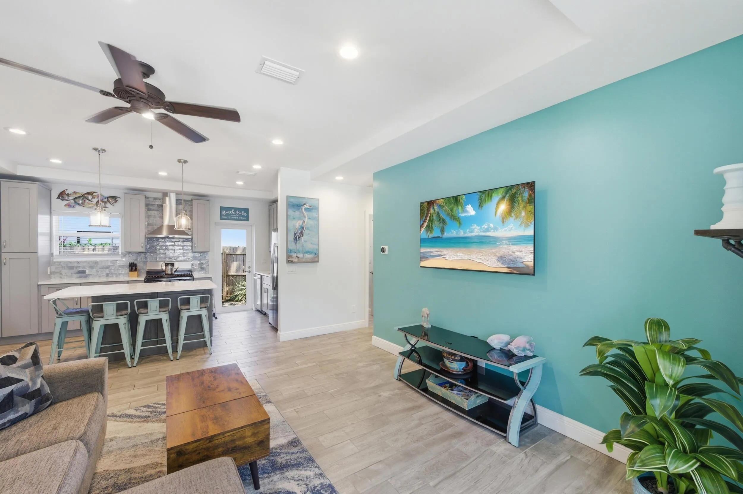 Open-concept living area featuring wood-finish flooring, recessed lighting, a modern ceiling fan, a kitchen island with seating, and a full kitchen with stainless steel appliances