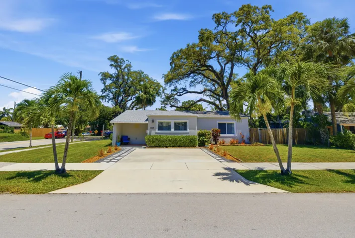 Single-story residence featuring a paved driveway, manicured lawn, and mature palm trees