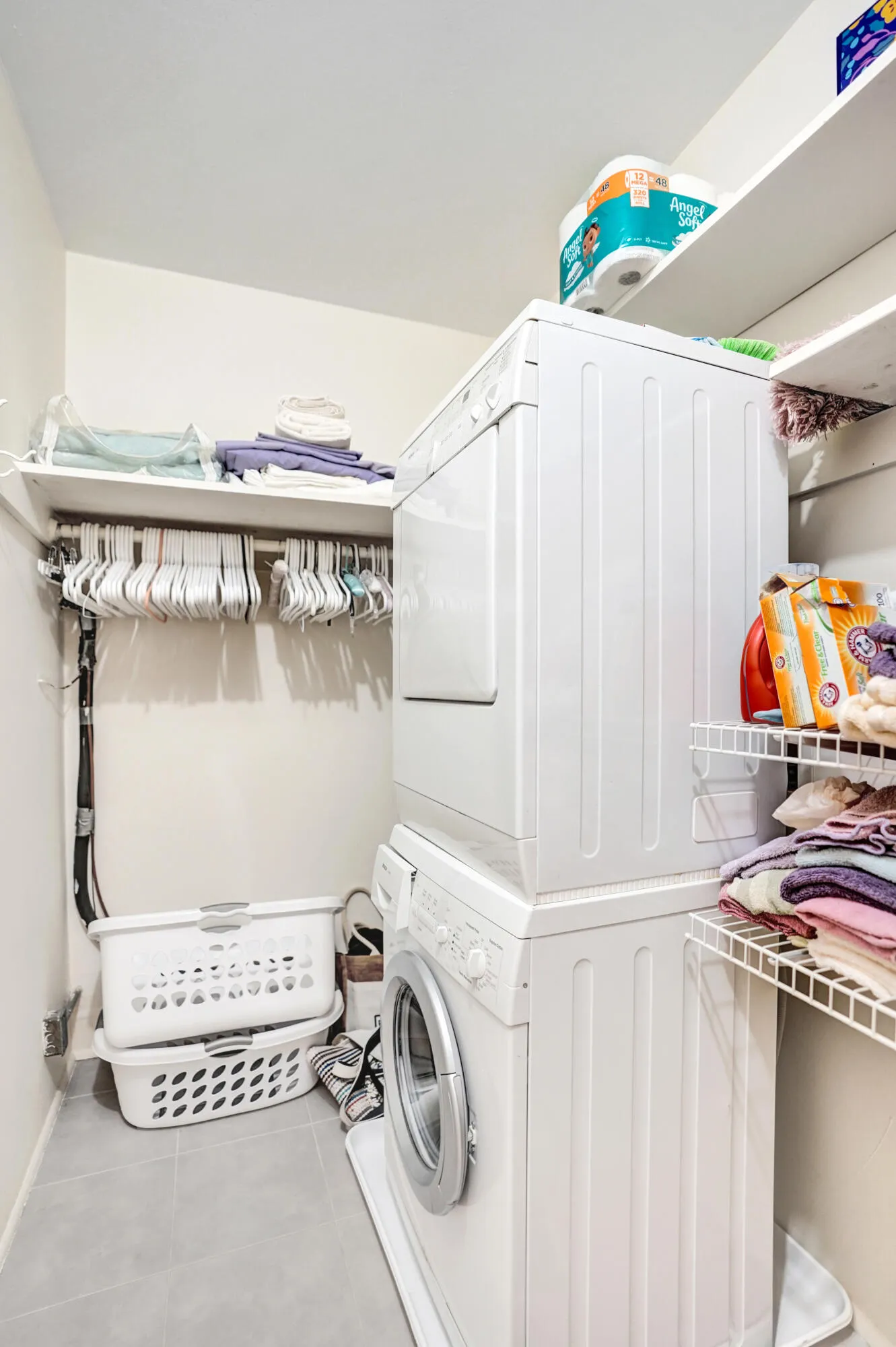Dedicated laundry area featuring a stacked washer and dryer, integrated wire shelving, and durable tile flooring