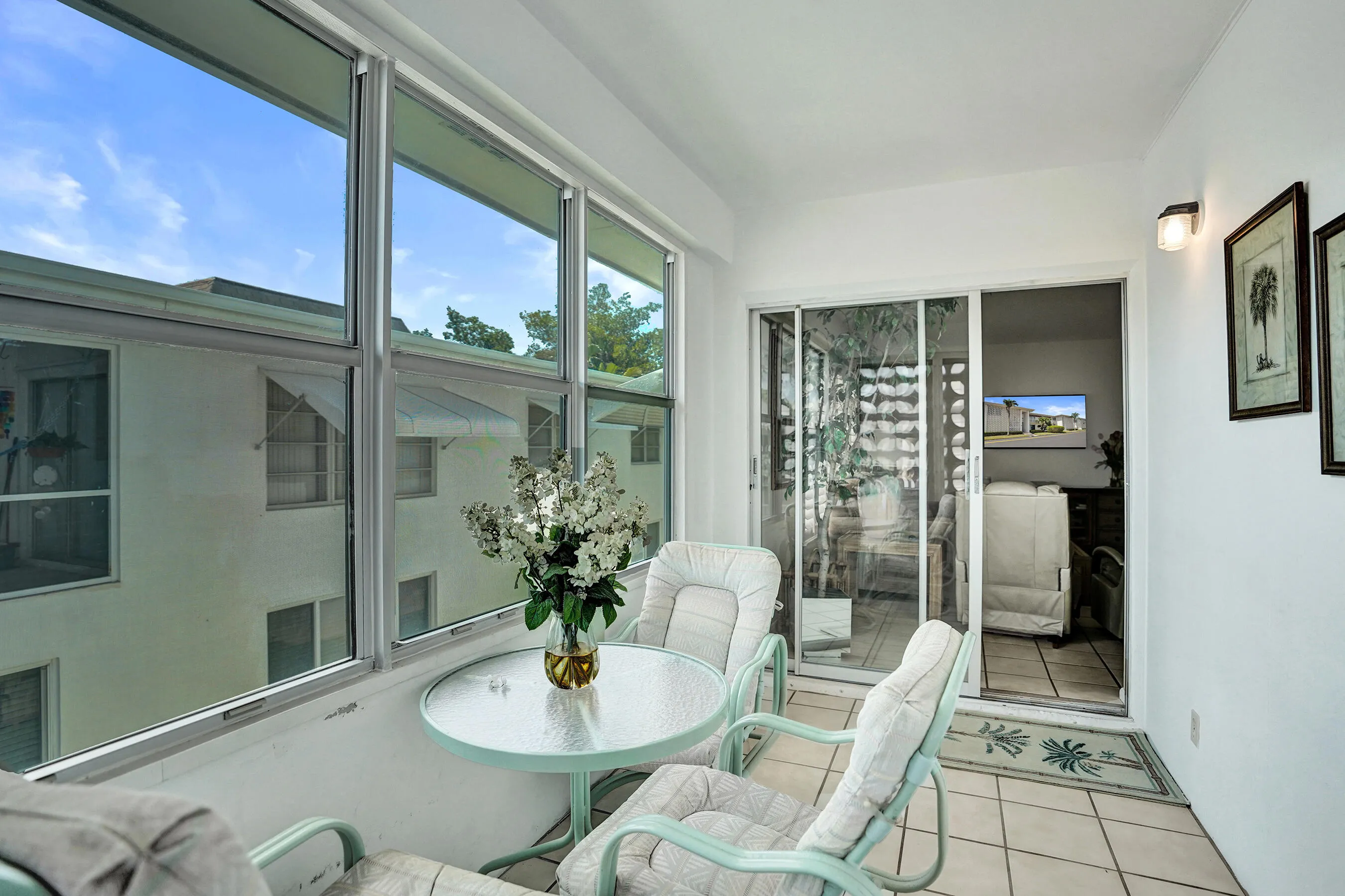 Enclosed patio featuring wall-to-wall windows, sliding glass door, white tile flooring, and a wall-mounted sconce