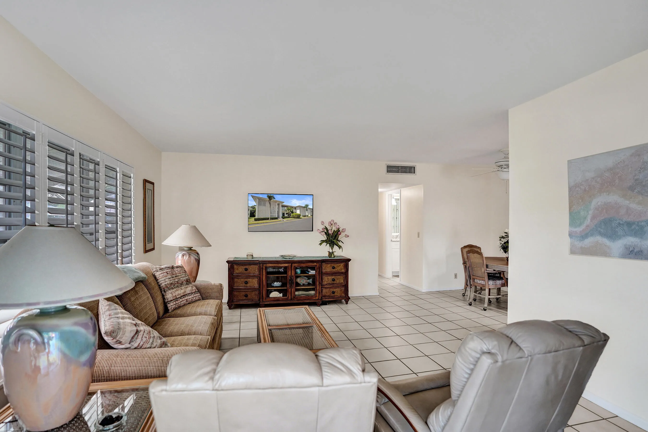 Spacious living area featuring neutral wall tones, tile flooring, and a large window with plantation shutters