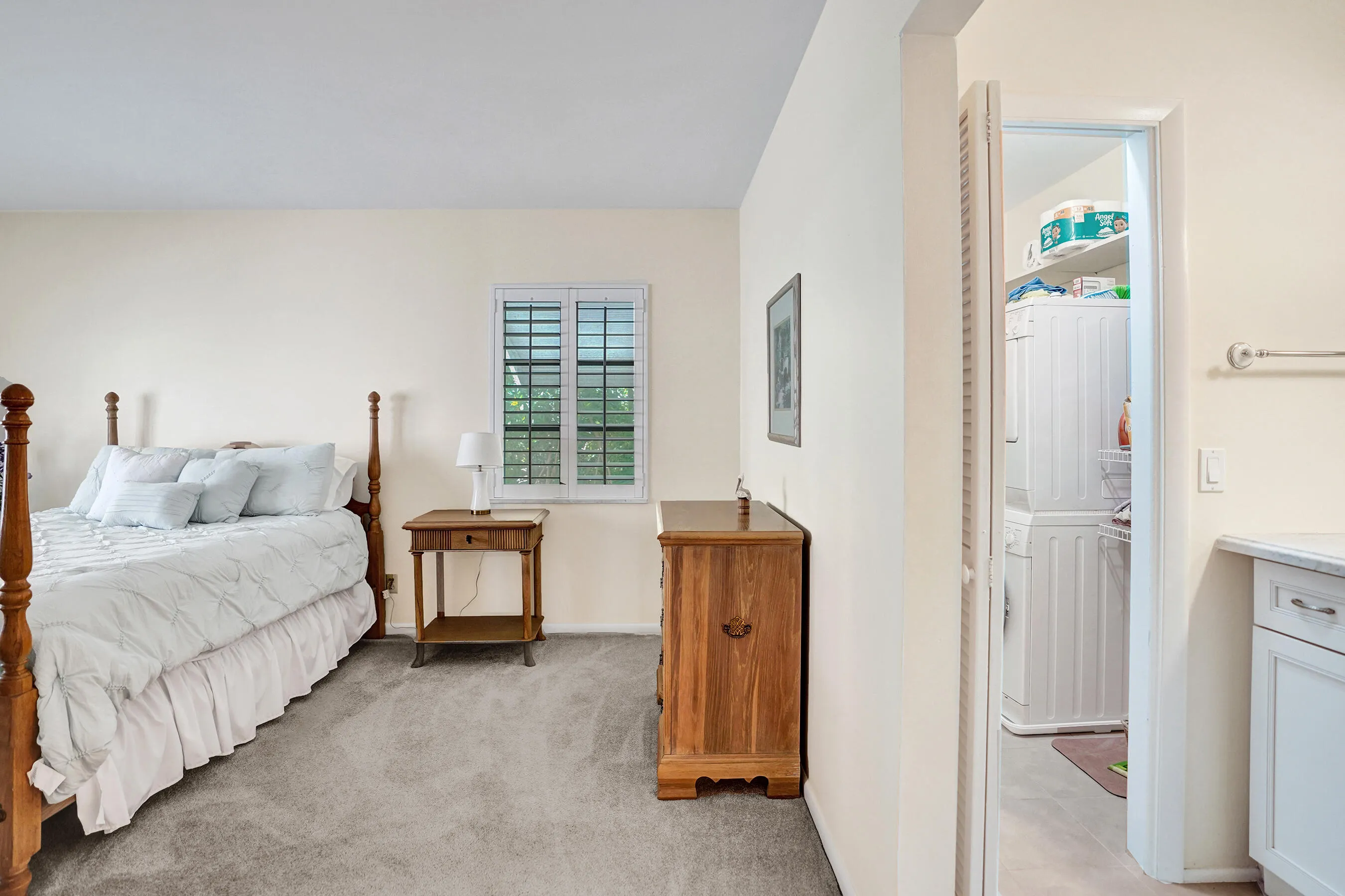 Well-lit room with light neutral wall paint, gray carpet, and a window featuring white plantation shutters