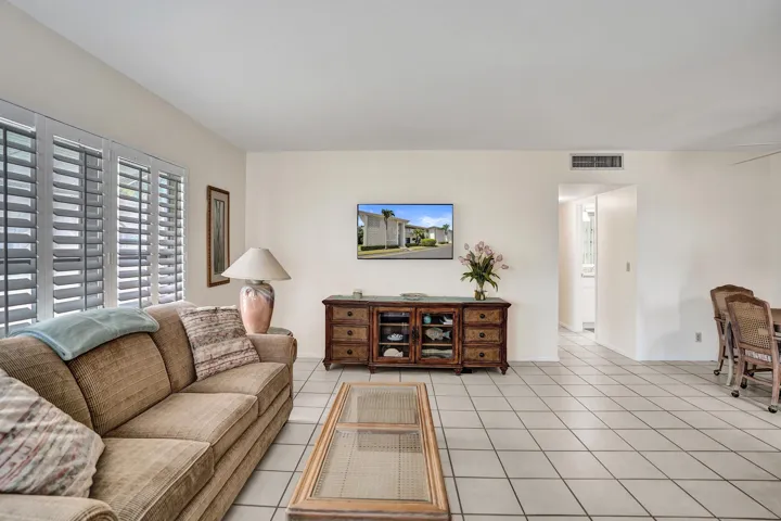 Large living area featuring white tile flooring, plantation shutters, and a wall-mounted display