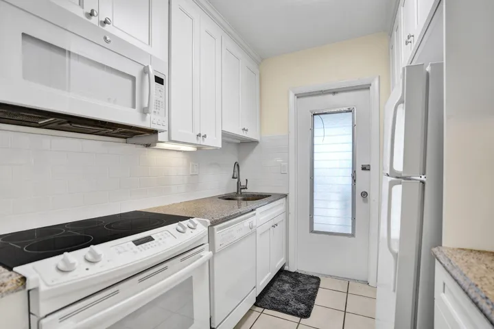 Kitchen featuring white cabinetry with silver hardware, speckled countertops, and a white subway tile backsplash
