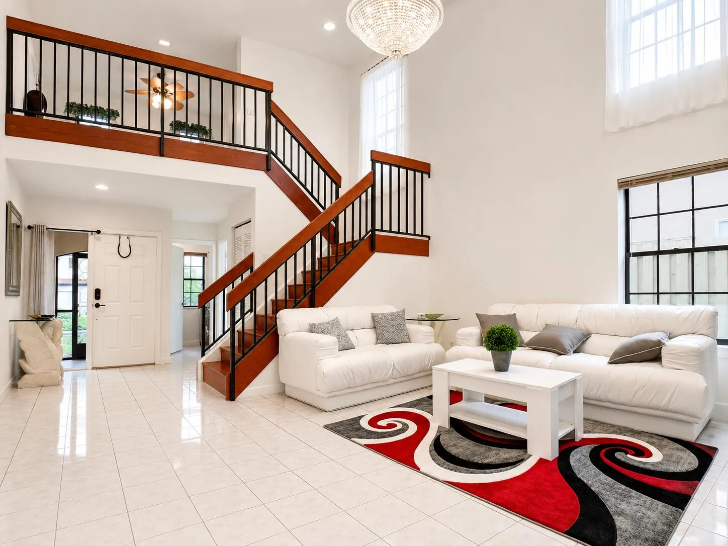 Two-story foyer featuring a grand staircase with wood-finish treads and black iron balusters, a second-story interior balcony, and an overhead chandelier