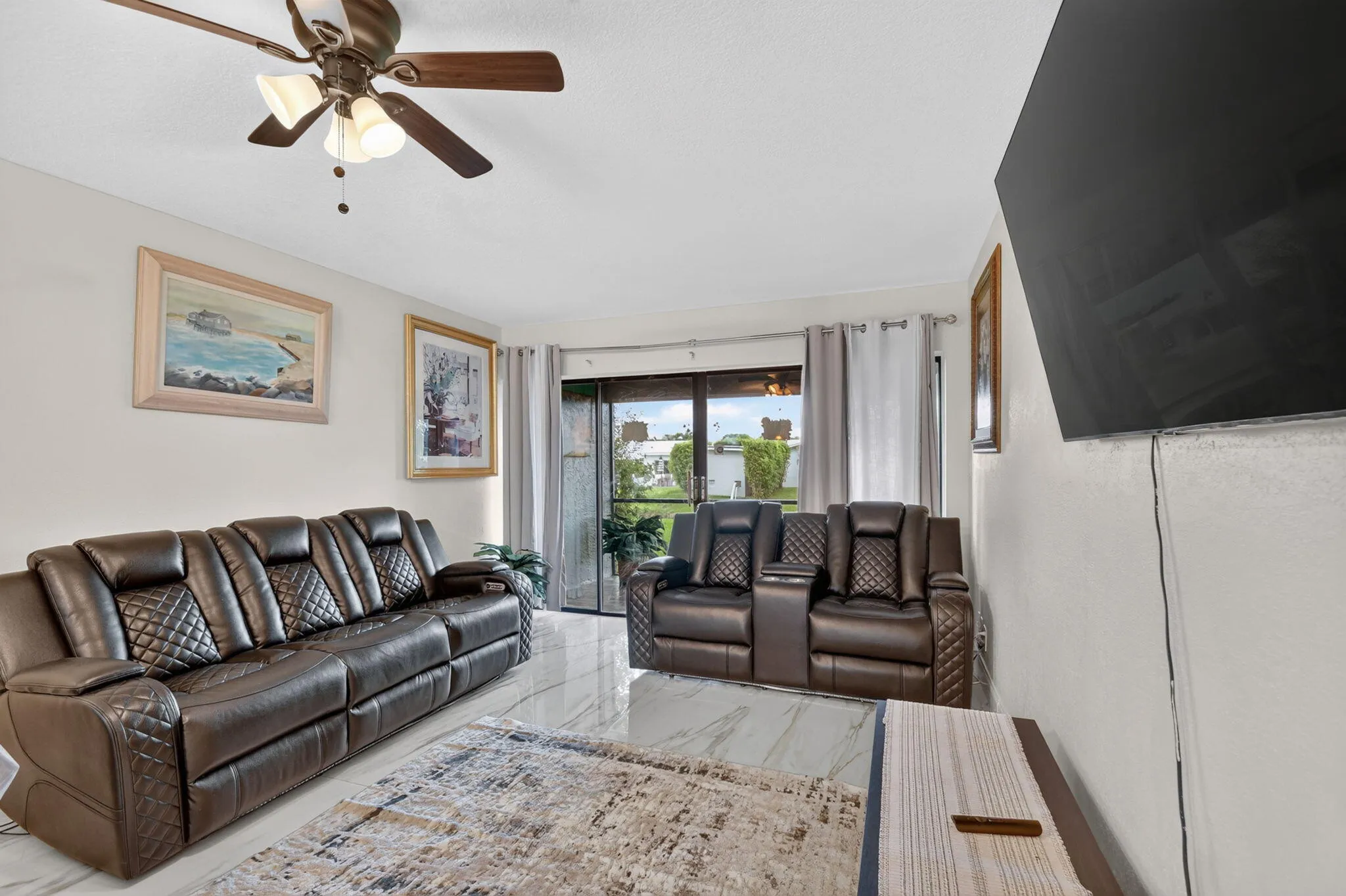 Spacious living area featuring polished tile flooring, a ceiling fan with integrated lighting, and white walls
