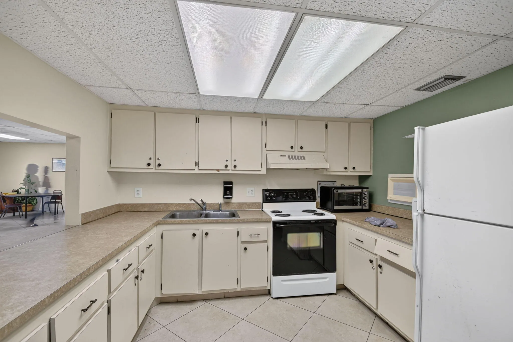 Kitchen area featuring extensive counter space, ample cabinetry, a double basin sink, electric range, and tile flooring