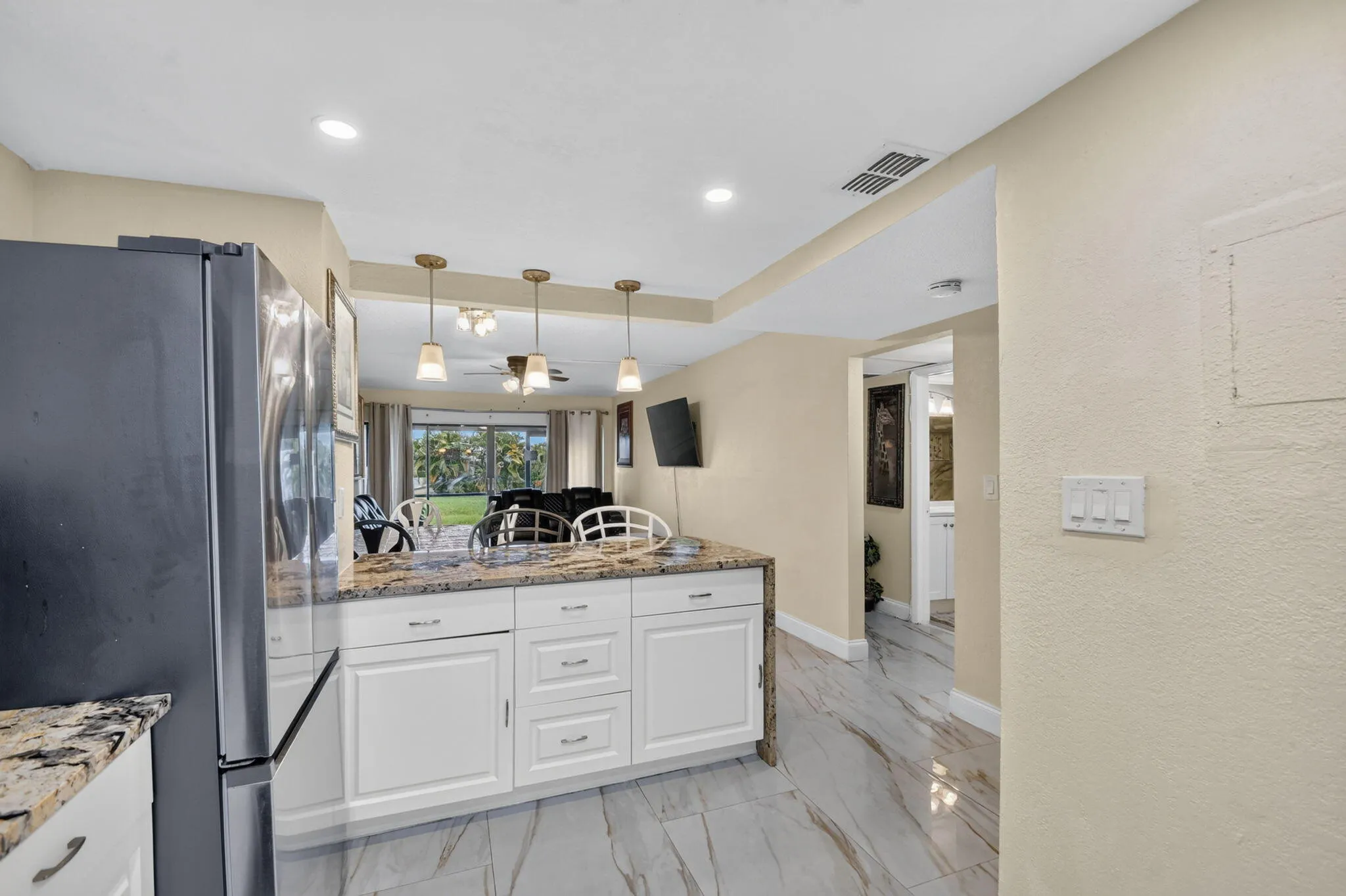 Kitchen island featuring white cabinetry with brushed nickel hardware, a granite countertop, and three pendant lights
