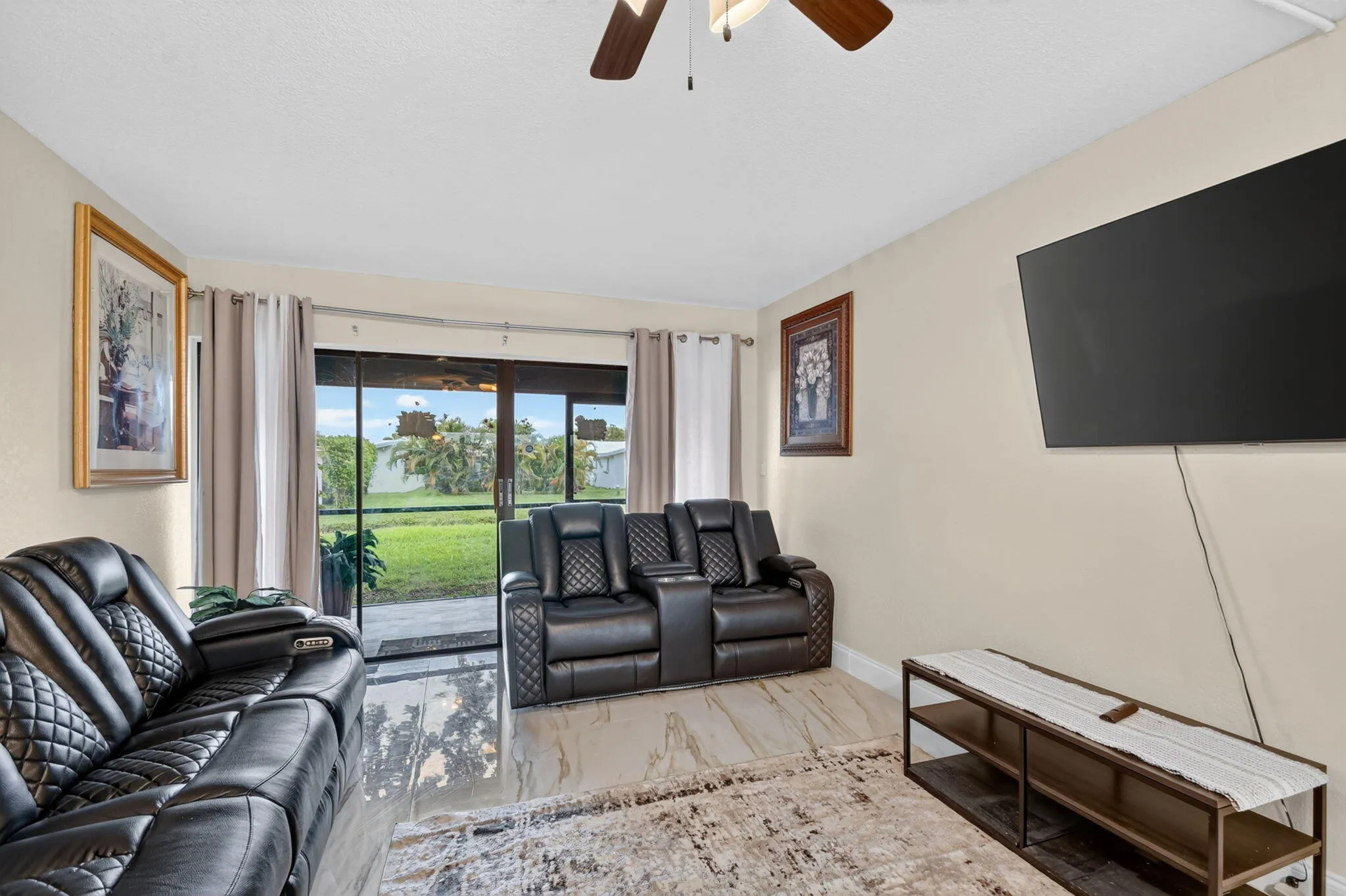 Spacious living area featuring neutral-toned walls, tiled flooring, and a ceiling fan
