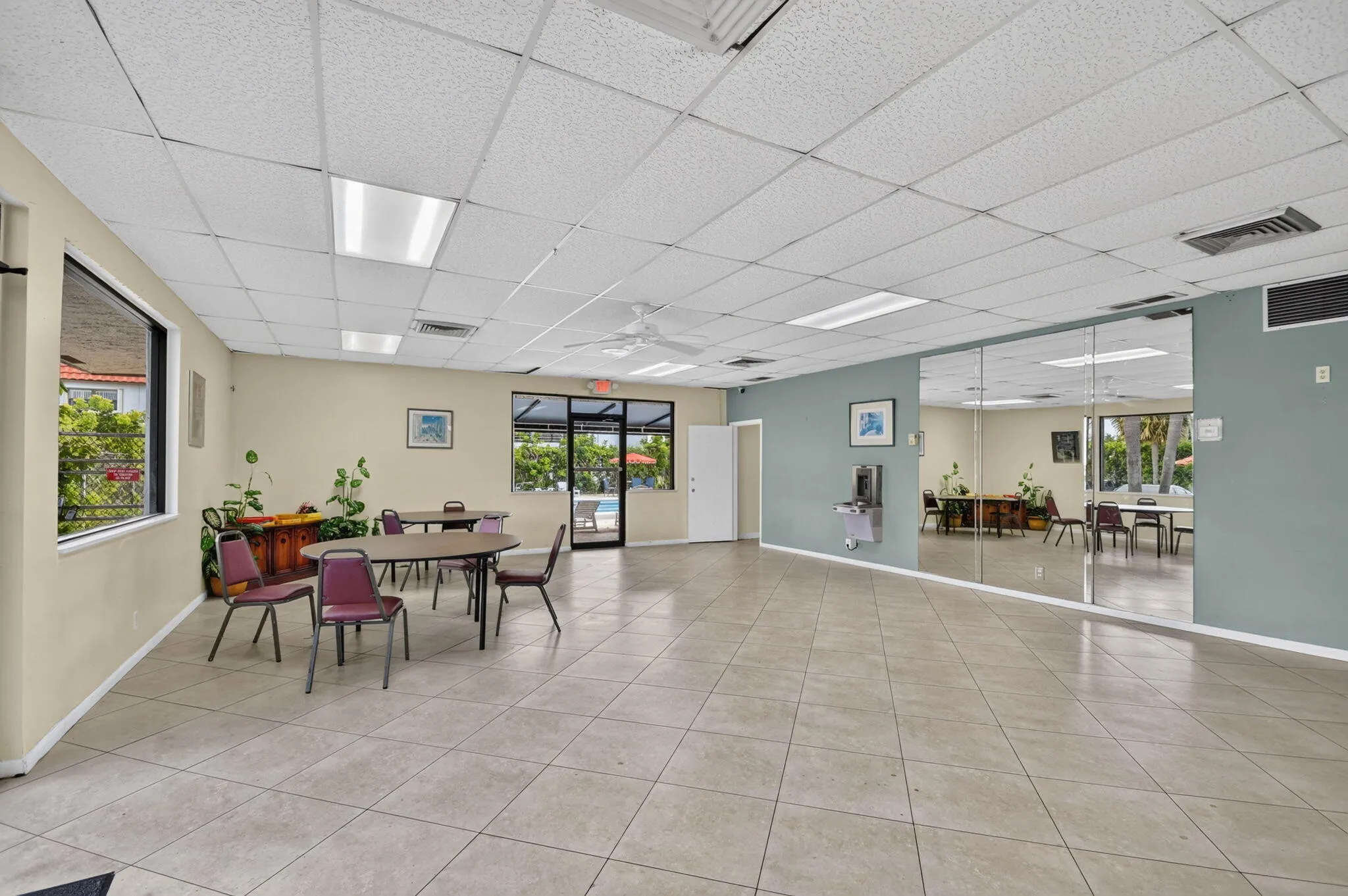 Spacious common area featuring light-toned tile flooring, drop ceiling with integrated lighting, and a mirrored wall
