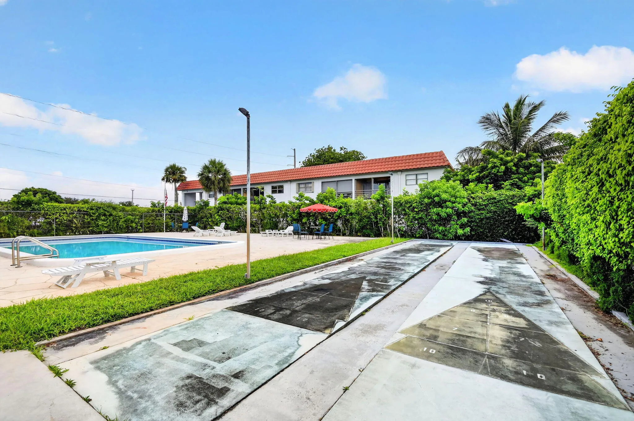 Outdoor recreational area featuring a swimming pool, concrete pool deck, green lawn, and two shuffleboard courts