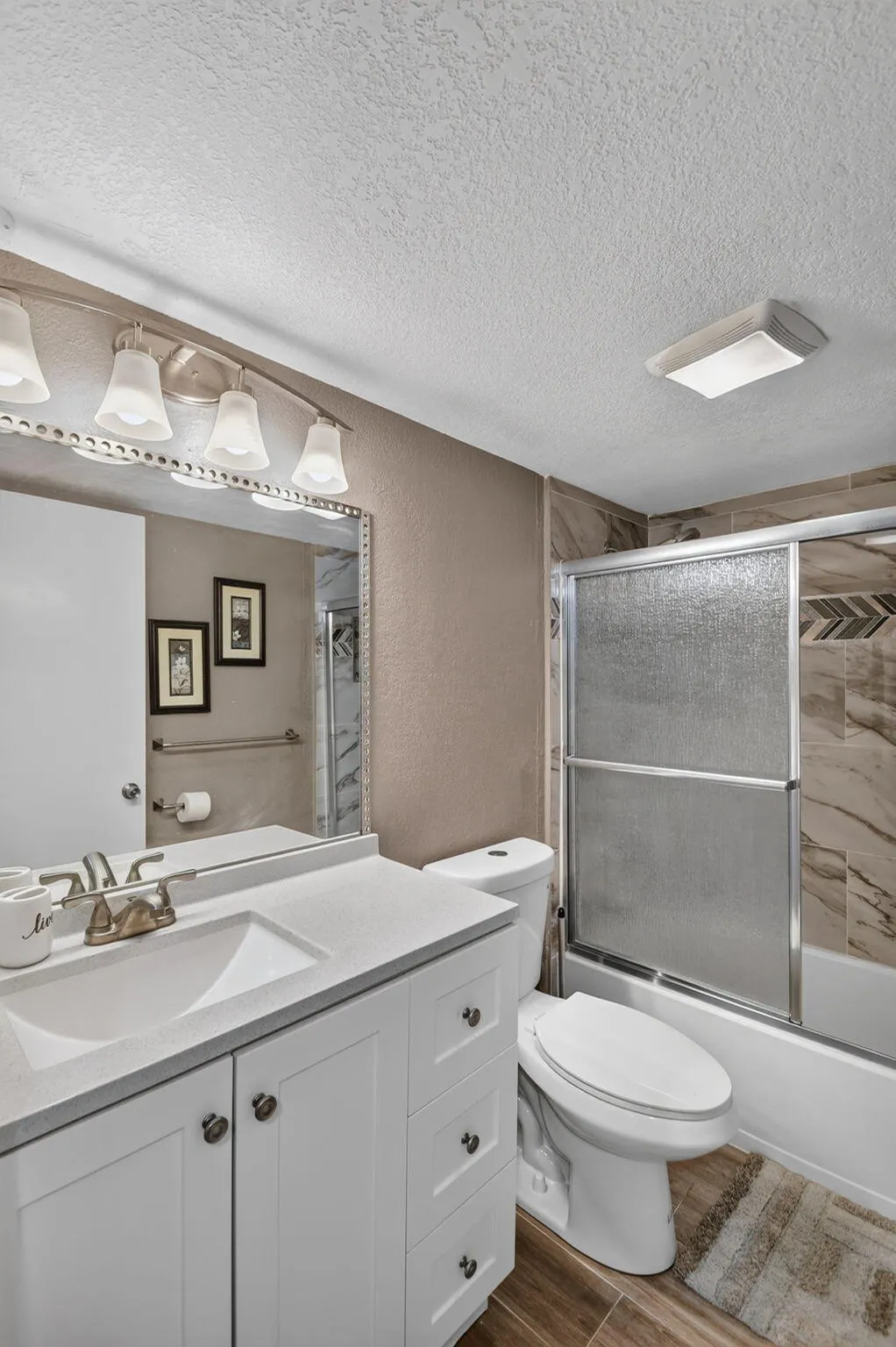 Bathroom featuring a single vanity with white cabinetry and a light-toned countertop, a shower-tub combination with sliding glass doors, and wood-finish flooring