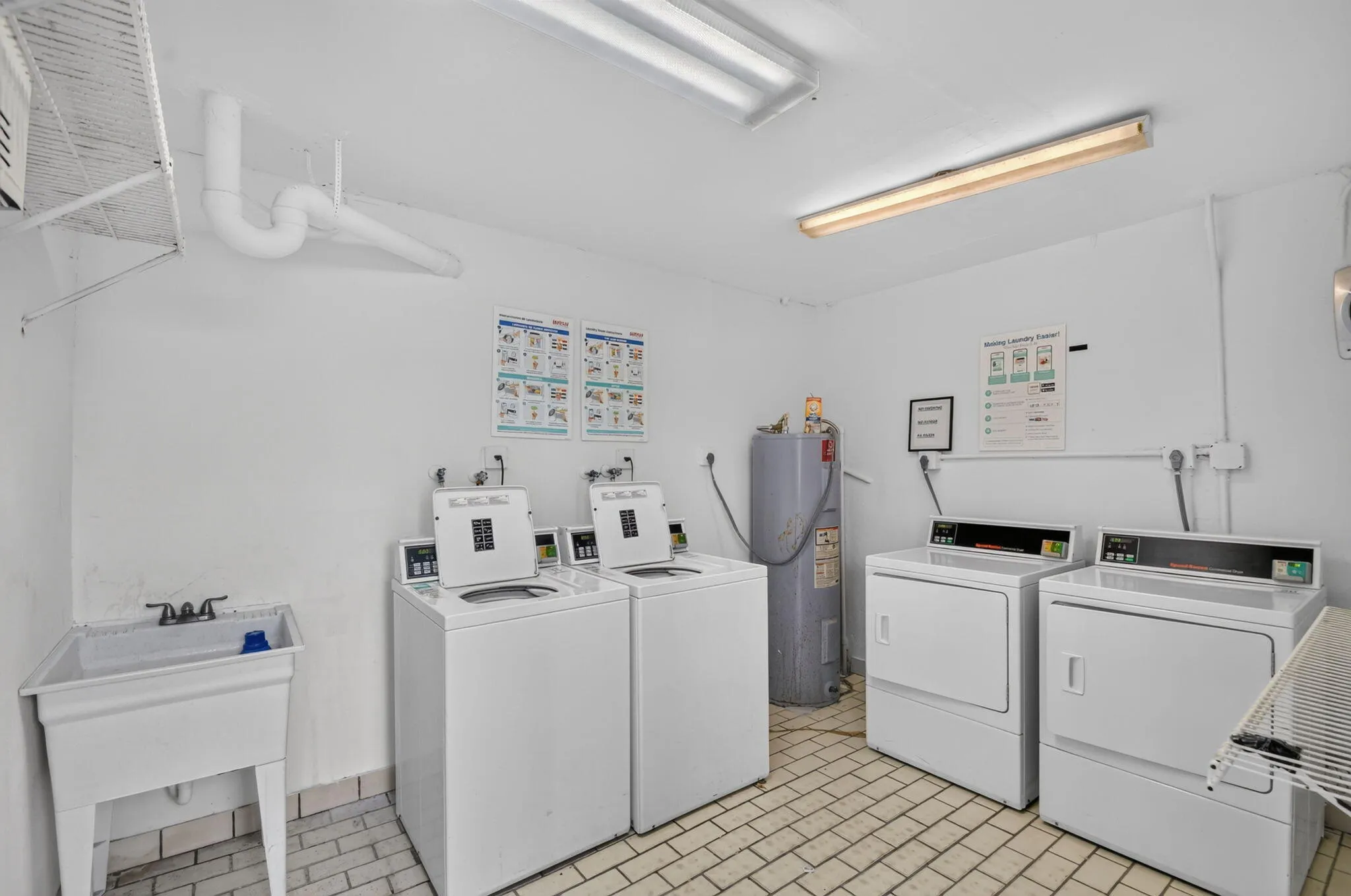 Dedicated laundry room featuring multiple washing machines and dryers, a utility sink, and tiled flooring