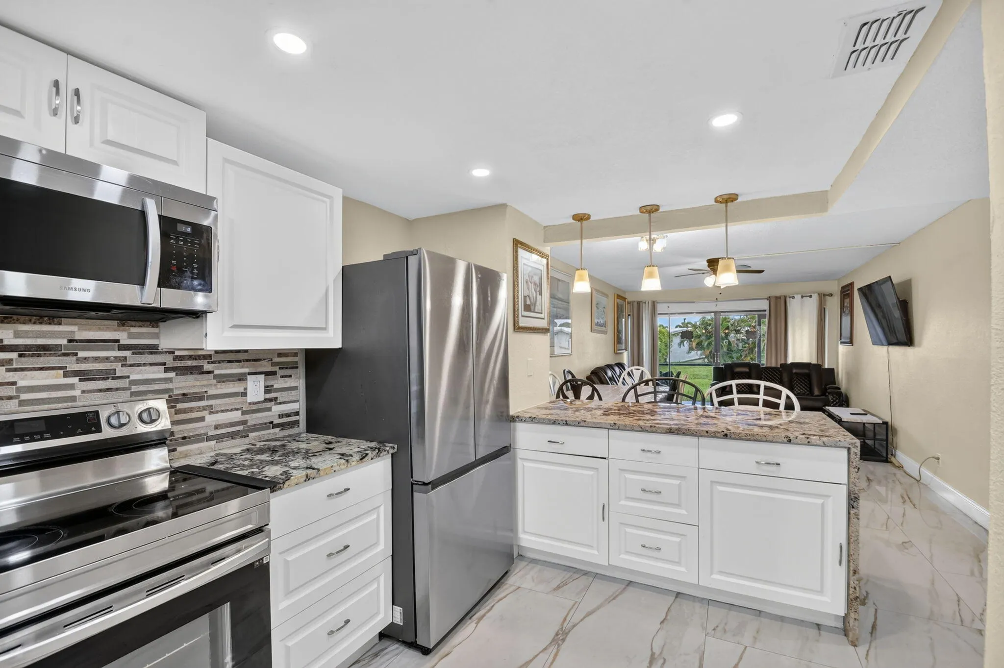 Kitchen featuring white cabinetry, stainless steel appliances, a multi-tone tile backsplash, and a granite-finish island with pendant lighting