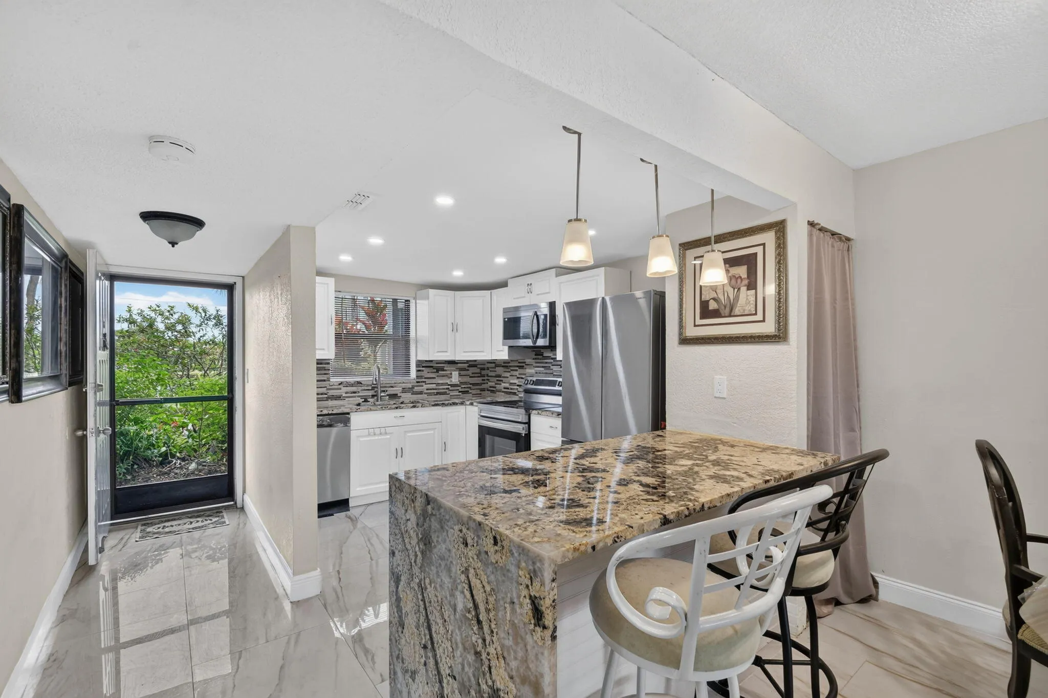 Kitchen featuring a granite-topped island with pendant lighting, white cabinetry, a mosaic tile backsplash, and stainless steel appliances